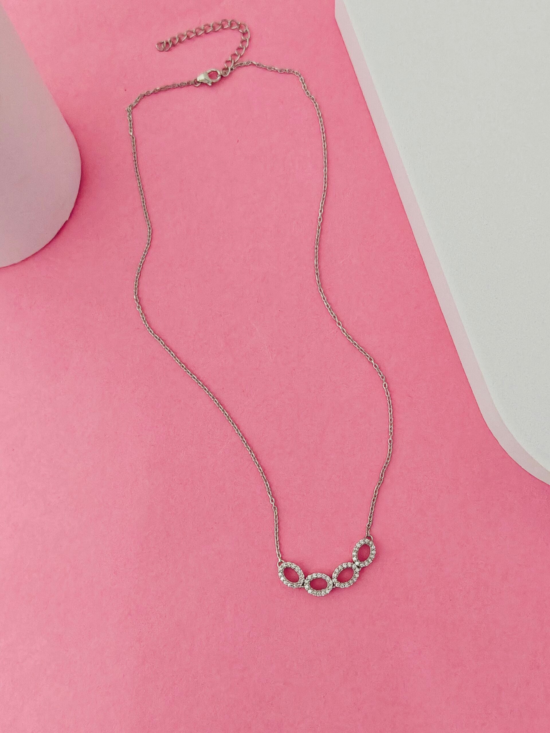 Silver necklace with circular design on a pink surface